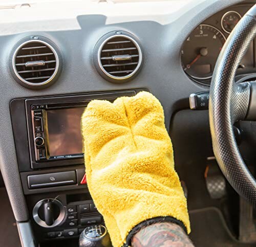 Person cleaning car dashboard with yellow glove.