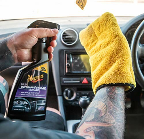 Person cleaning car interior with detailing spray and cloth